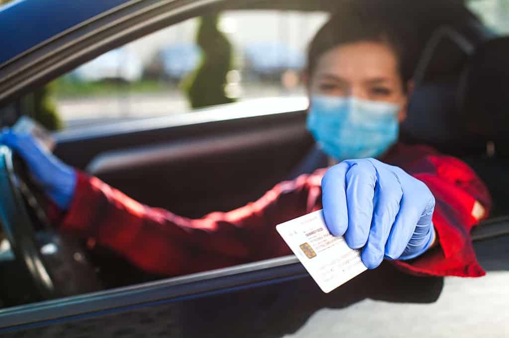 Young female driver showing Coronavirus health card or immunity passport
